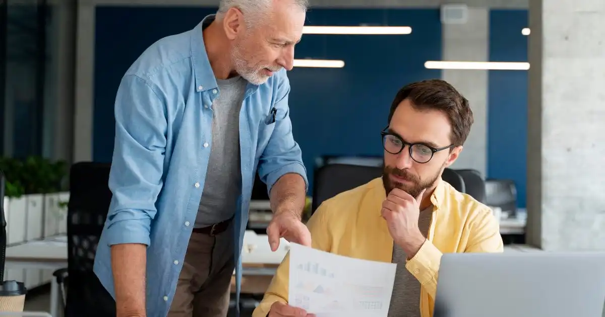 Older man showing a report to a younger colleague in the office.